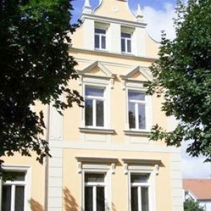 Ansicht eines hellen, gepflegten historischen Stadthauses mit weiß abgesetzten Fensterumrandungen und dekorativem Giebel.