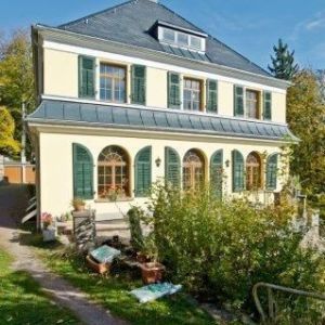 Prachtvolle sanierte Villa mit hellgelber Fassade, grünen Fensterläden und einem Mansarddach.