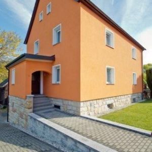 Modern sanierte Fassade in kräftigem Orange mit neuen weißen Fenstern und überdachtem Eingangsbereich.