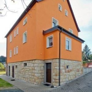 Giebelansicht eines zweistöckigen Wohnhauses mit frischem orangefarbenem Putz und dunklen Dachrinnen.