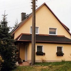 Ein schlichtes Einfamilienhaus mit gelber Fassade, zwei quadratischen Fenstern im Obergeschoss und einem dunklen Satteldach.
