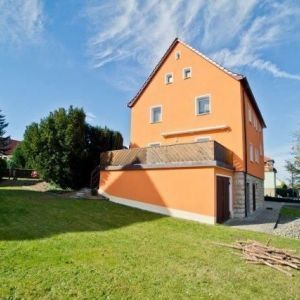 Außenansicht eines sanierten Wohnhauses in Orange mit Balkon und angrenzendem Gartenbereich.