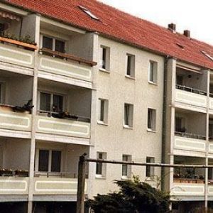 Mehrstöckiges Wohnhaus mit Balkonen, heller Fassade und einem roten Ziegeldach. Die Architektur wirkt funktional und modern.