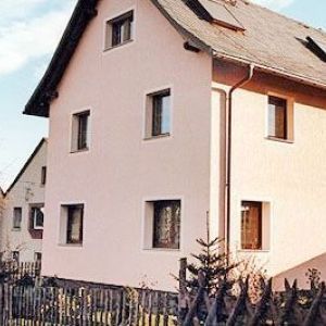 Seitenansicht eines rosa-beigen Hauses mit dunklem Dach und braunen Fensterrahmen unter klarem Himmel.