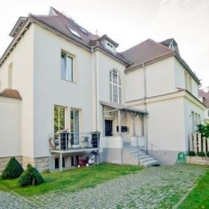 Giebelansicht eines sanierten Wohnhauses in Orange mit großem Balkon und dunklen Dachrinnen.