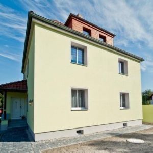 Sanierte Fassade eines Mehrfamilienhauses in hellem Grün mit modernen Fenstern und rotem Ziegeldach.