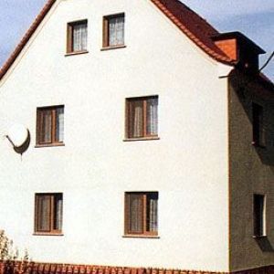 Giebelansicht eines hellen Hauses mit unregelmäßig angeordneten Fenstern und einer kleinen Dachgaube auf der rechten Seite.