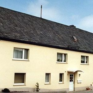 Gelbes Haus mit blauem Dach und Sonnensegel über der Terrasse.