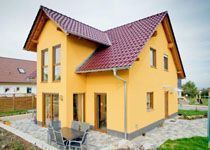 Zweistöckiges gelbes Wohnhaus mit markantem Giebel, roten Dachpfannen und modernen Fenstern in einer Siedlung.