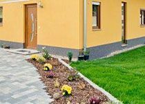 Gepflegter Hauseingang mit gepflastertem Weg, kleiner Rabatte mit Rindenmulch und einer modernen Haustür.