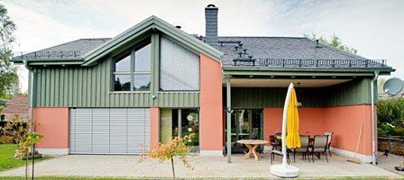 Modernes Einfamilienhaus mit einer Kombination aus grüner Holzverkleidung, rotem Putz und großen Glasflächen.