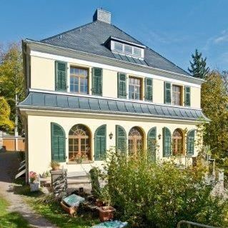 Seitenansicht eines gelben Hauses mit dunkelblauem Ziegeldach.