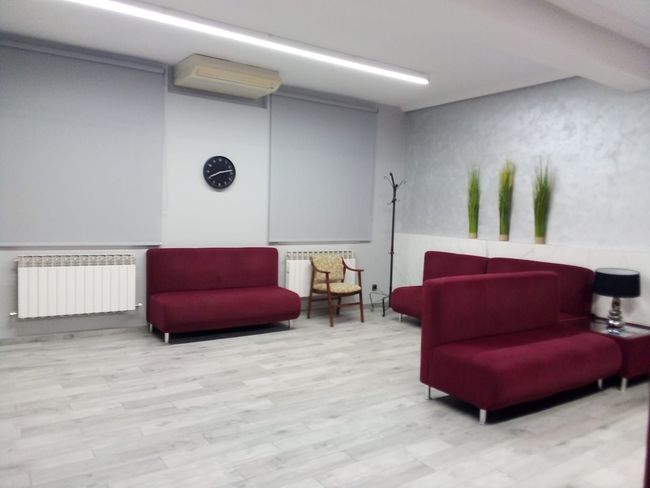 Una sala de espera con sofás rojos y un reloj en la pared.