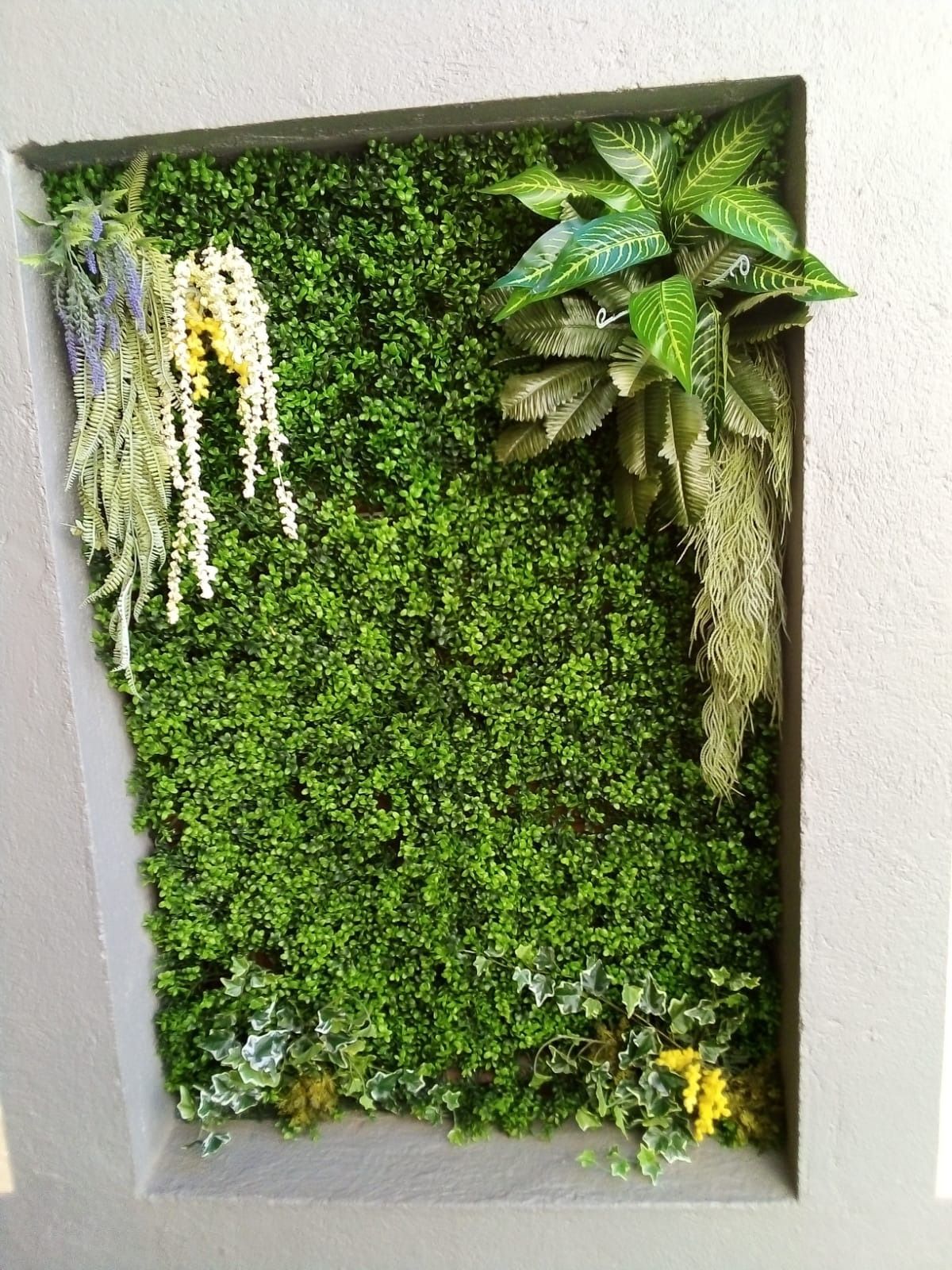 Una imagen de una pared verde con plantas y flores.
