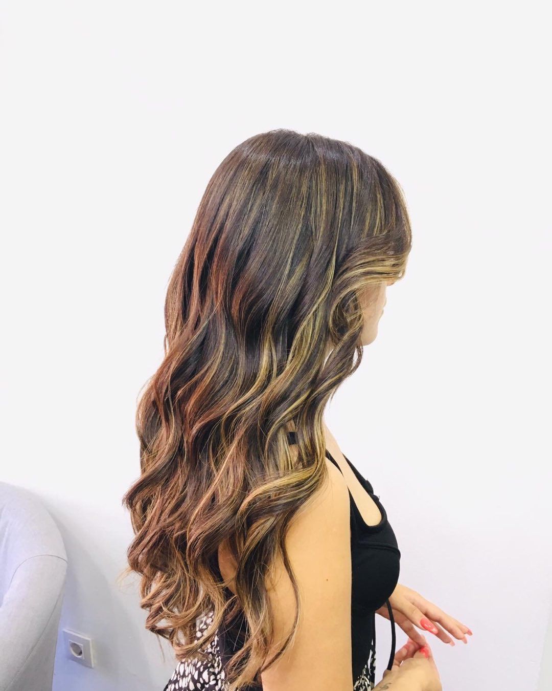 Vista lateral de una larga melena castaña ondulada con reflejos rubios, peinada sobre un fondo blanco liso.