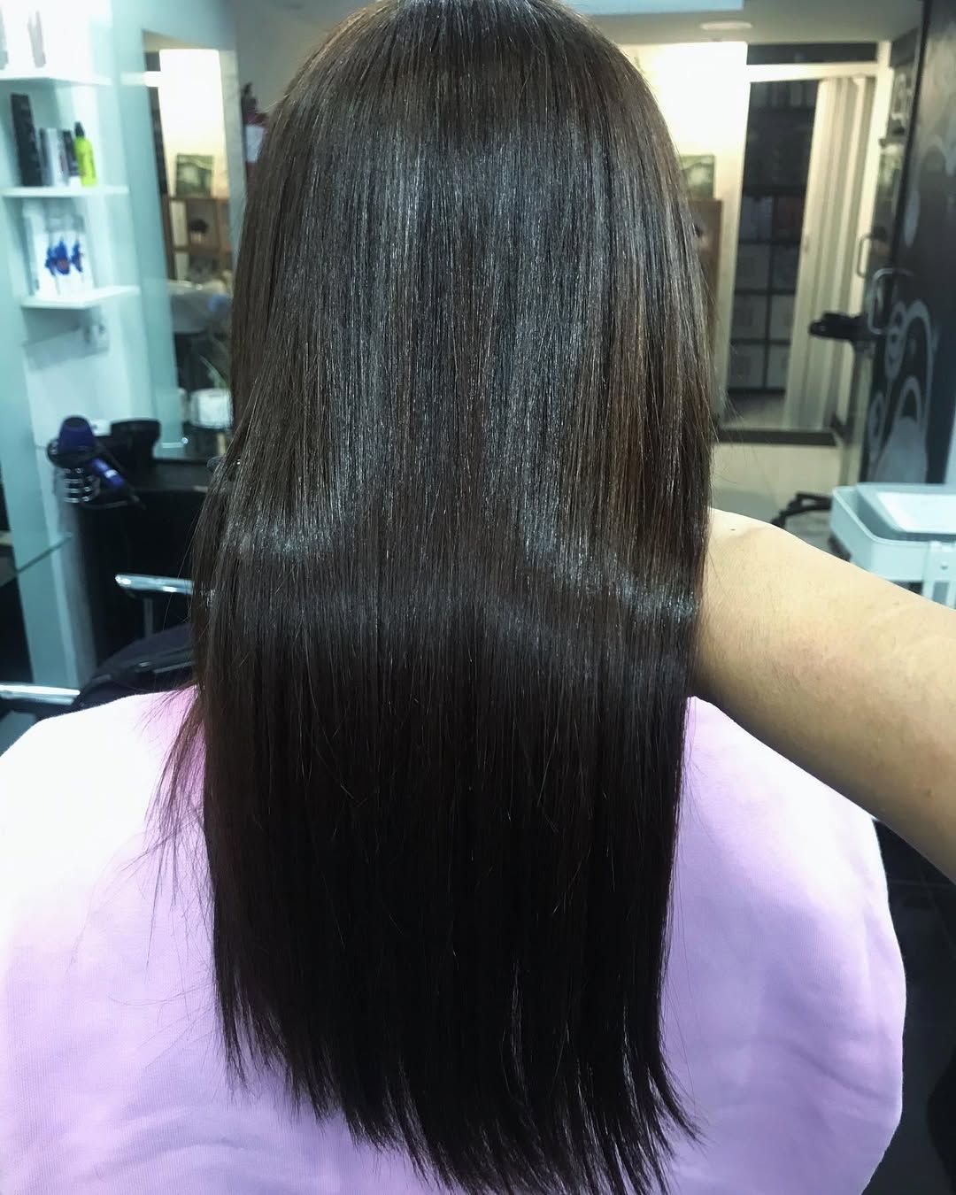 El cabello liso, castaño oscuro y hasta los hombros de una persona, visto desde atrás en un salón de belleza.