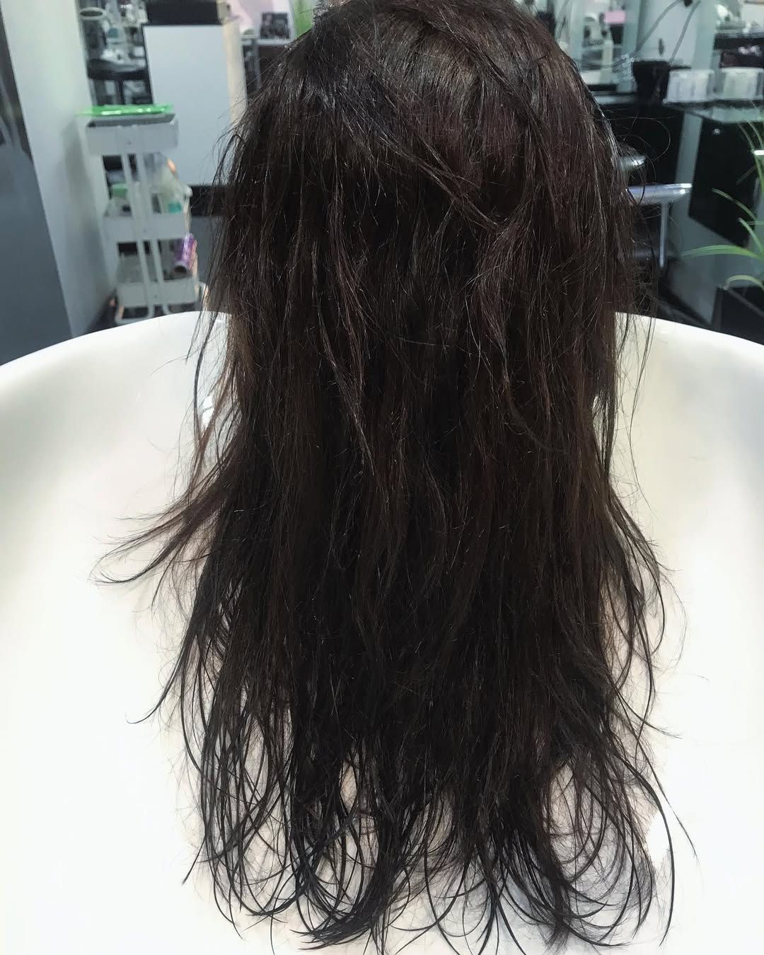 Una persona con el pelo largo, húmedo y castaño oscuro está sentada en el lavabo de una peluquería.