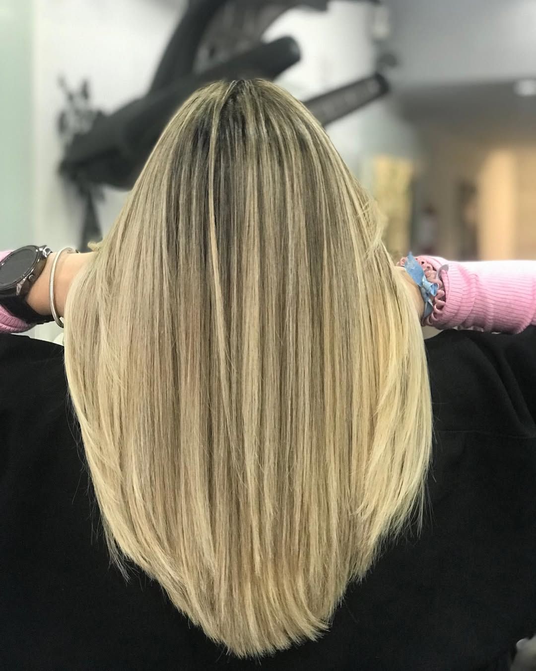 En una peluquería, una persona luce de espaldas una melena rubia lisa, hasta los hombros, con reflejos de varios tonos.
