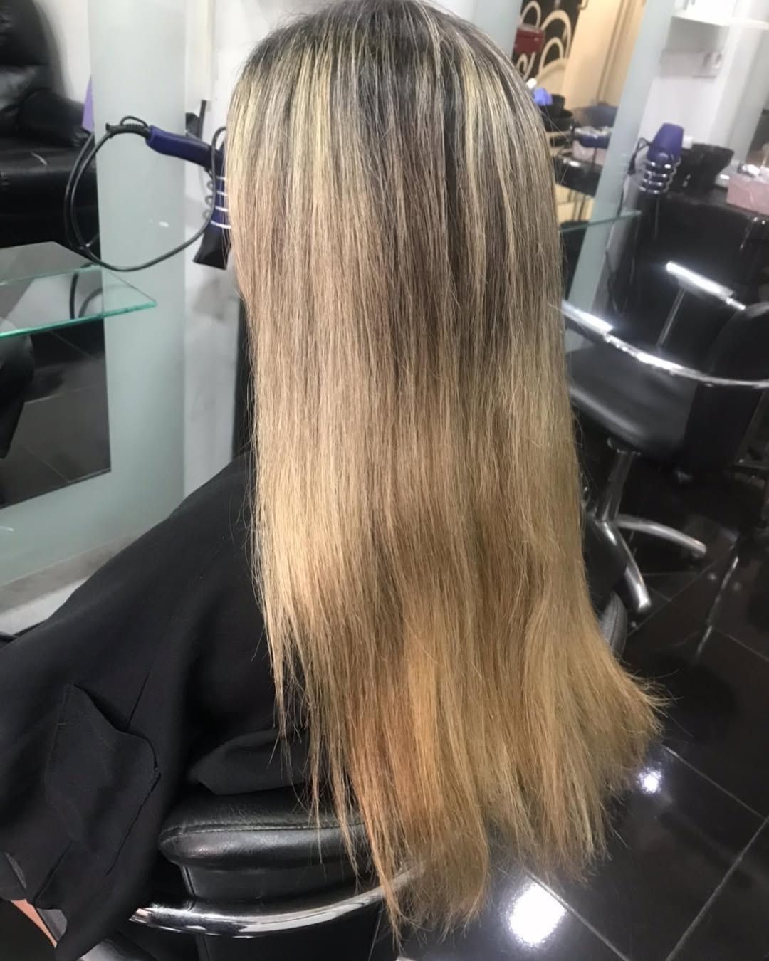 Una persona sentada en una silla de peluquería luce una melena larga con raíces oscuras que se van aclarando.