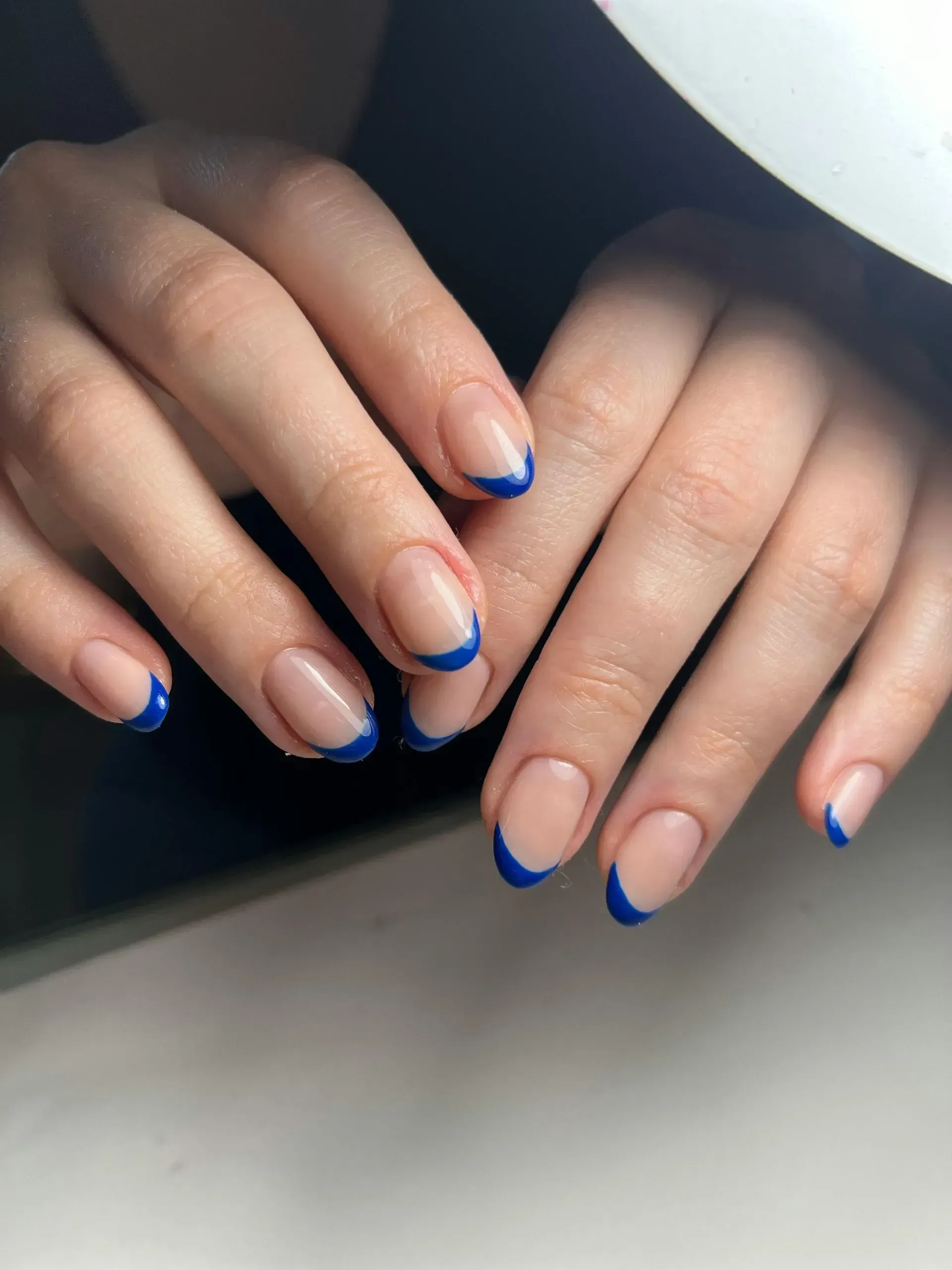 Primer plano de unas manos que muestran uñas almendradas con una manicura francesa de color azul.

