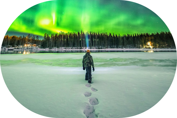 Mies kävelemässä järven jäällä katselemassa revontulia.