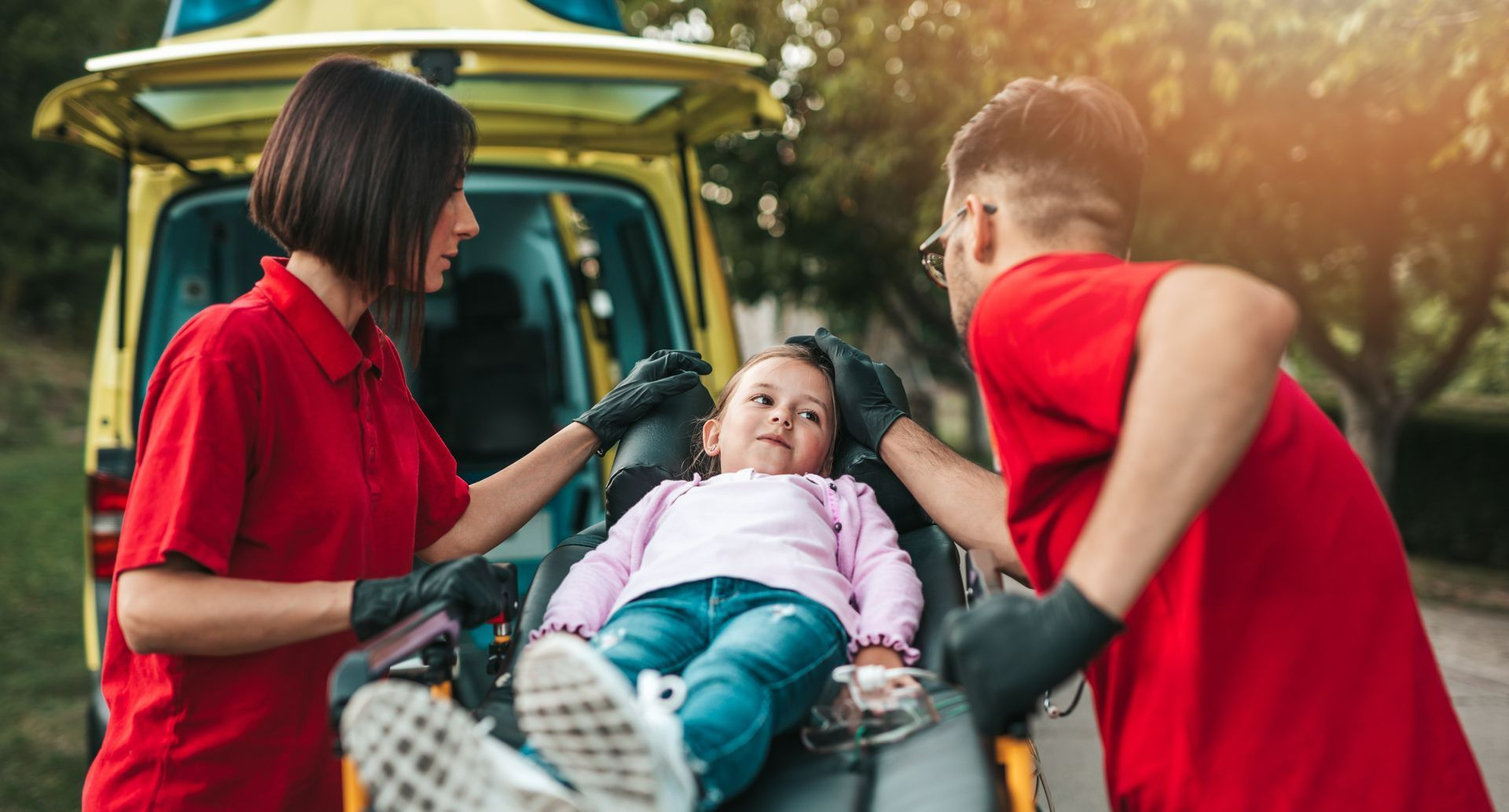 Une enfant entourée de deux ambulanciers avec des t-shirts rouges