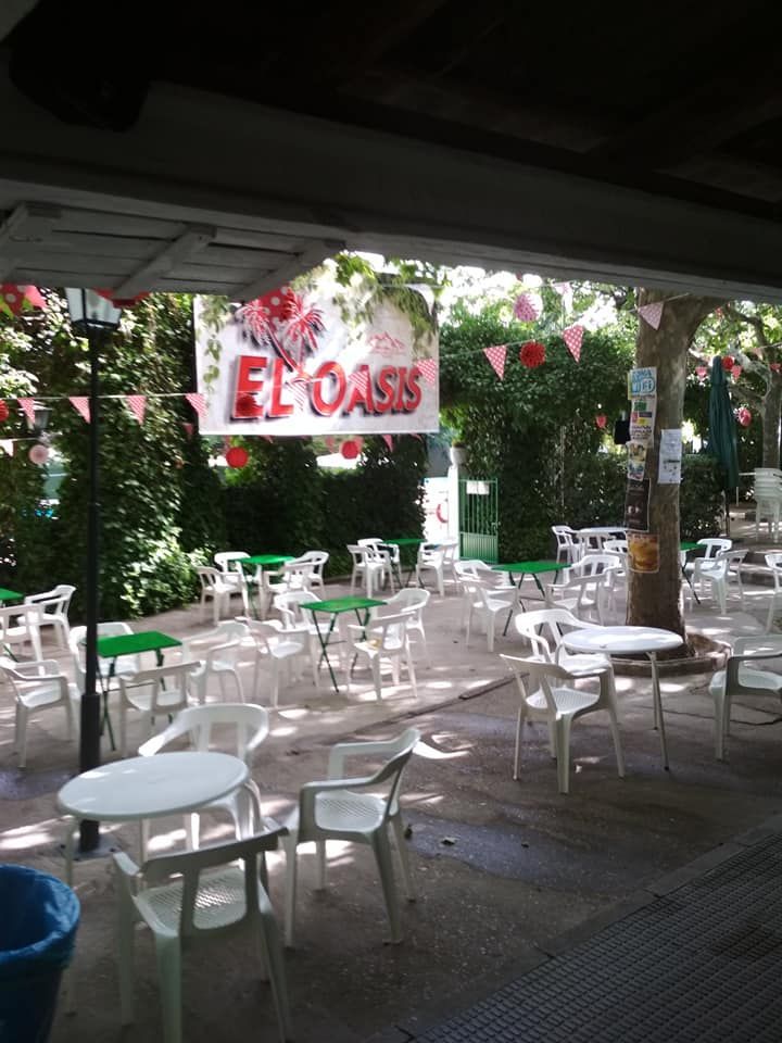 Un patio con mesas y sillas y un cartel que dice el oasis.