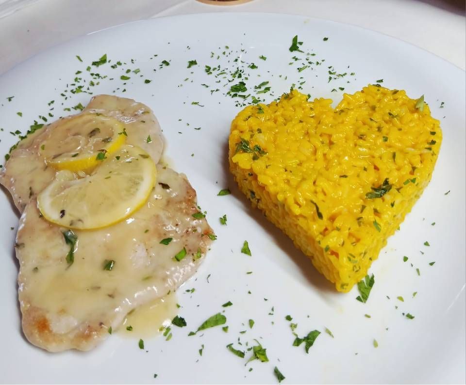 Hähnchen Piccata mit Zitronenscheiben und herzförmigem Safranreis, garniert mit Petersilie auf einem weissen Teller.