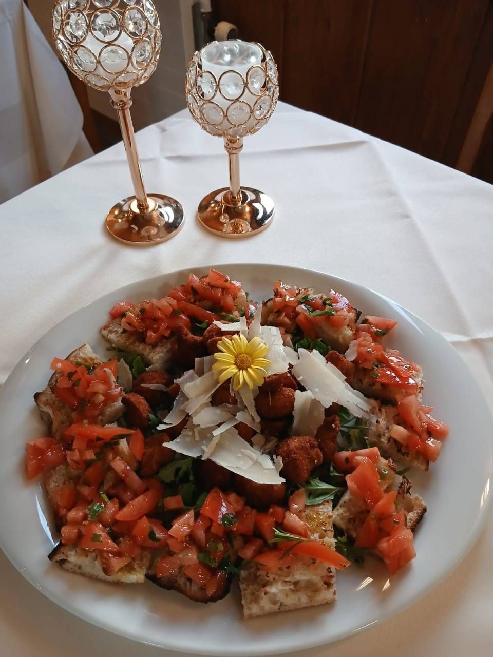 Bruschetta auf einem weissen Teller mit Tomaten, Käse und einer Blume; auf einer weissen Tischdecke.