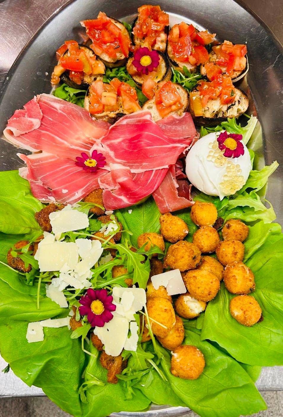 Vorspeisenplatte: Bruschetta, Prosciutto, Käse, frittierte Bällchen und Grünzeug auf einem Silbertablett.