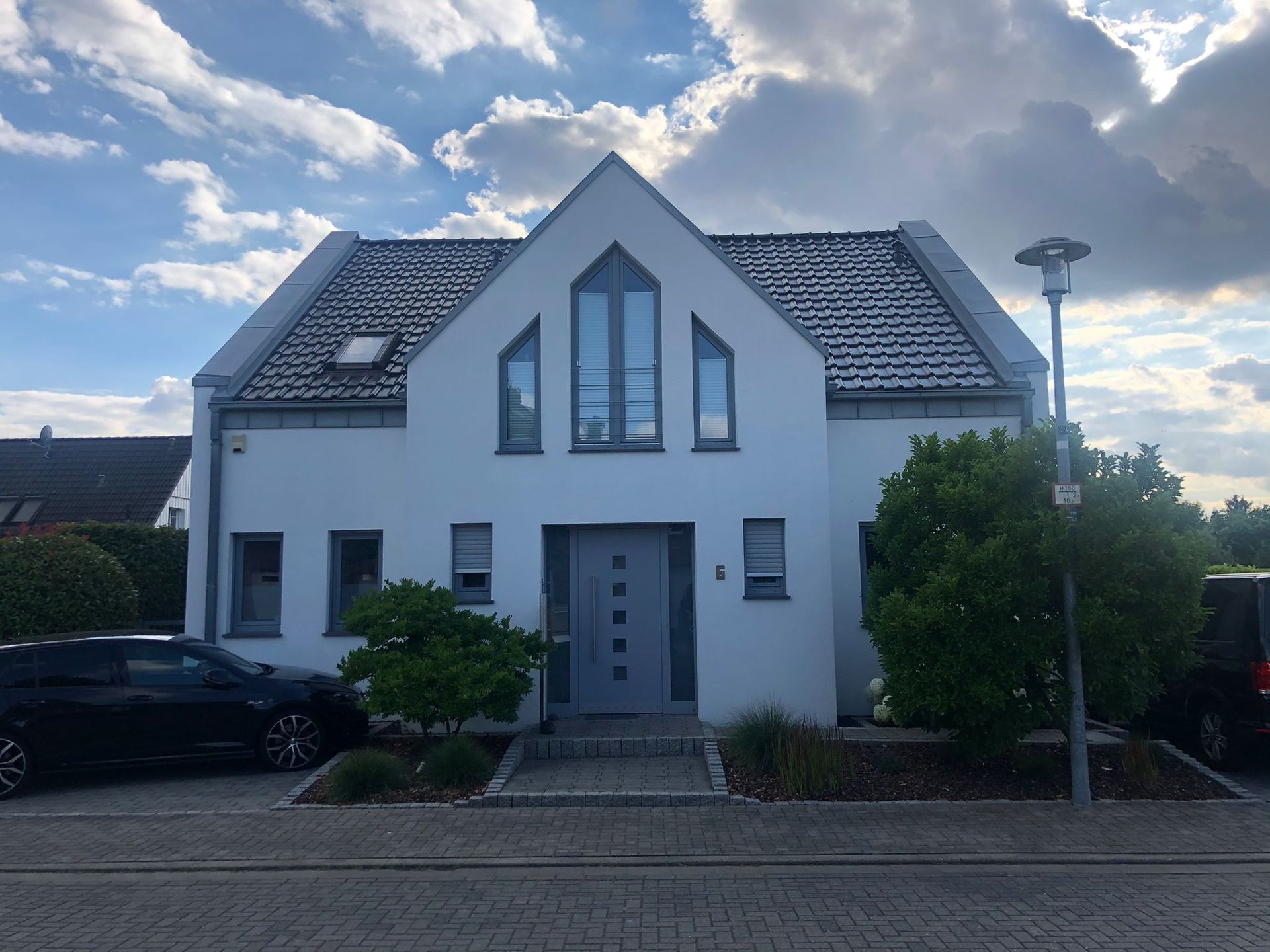 Weißes Haus mit grauem Dach, grauen Fenstern und grauer Tür. Ein schwarzes Auto parkt davor.