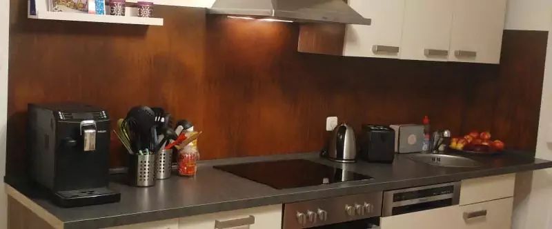 Küche mit Geräten wie Kaffeemaschine, Herd und Toaster. Brauner Fliesenspiegel, weiße Schränke und graue Arbeitsplatte.