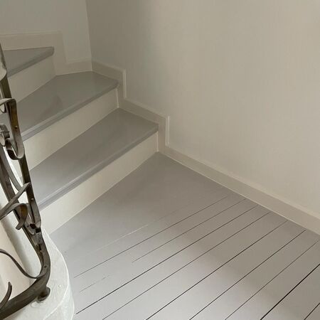 Treppe und Boden aus grau gestrichenem Holz, Wände und Zierleisten weiß. Metallgeländer links.