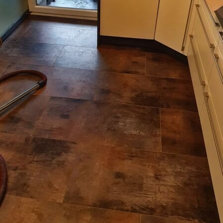 Braune Fliesen auf dem Küchenboden, im Hintergrund sind teilweise Schränke und eine Tür zu sehen.