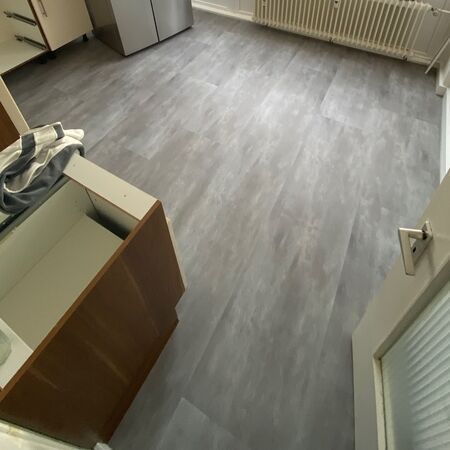 Küche mit grauem Boden und Schränken; offene Schranktür, sichtbarer Heizkörper und geschlossene Tür.