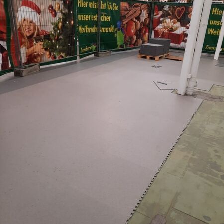 Grauer Boden in einem Baustellenbereich, im Hintergrund sind Weihnachtsdekorationen zu sehen.