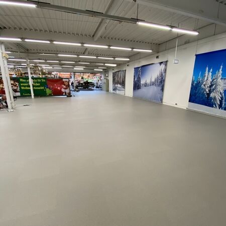 Leere, helle Ladenfläche mit grauem Boden. Große Wandbilder mit verschneiten Landschaften.