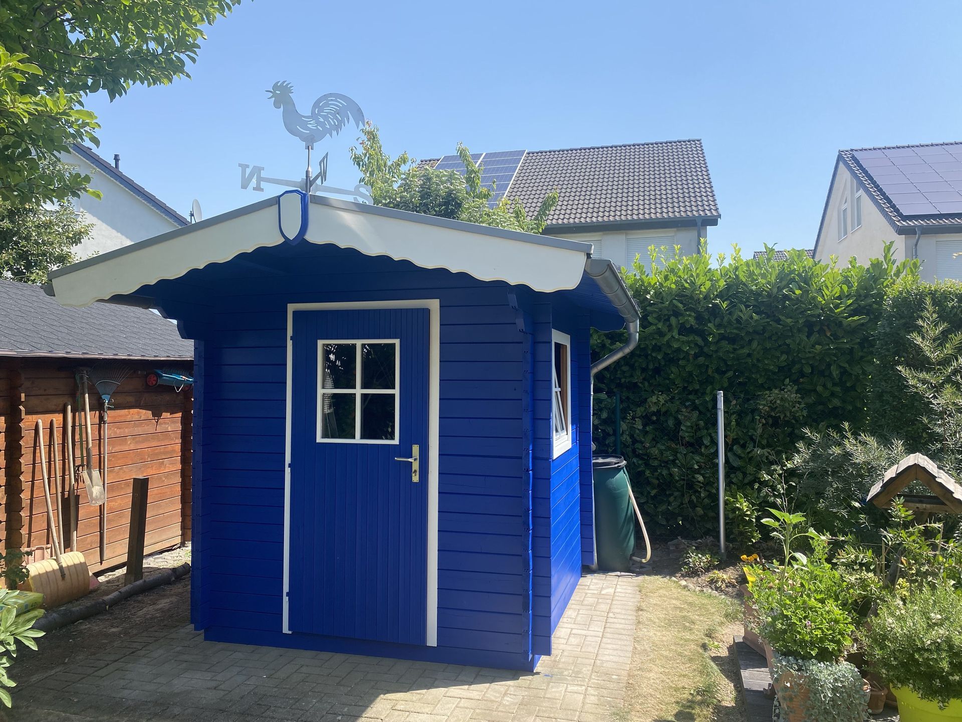 Ein blauer Holzschuppen mit weißen Zierleisten.