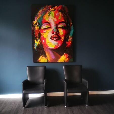 Farbenfrohes Gemälde von Marilyn Monroe über zwei schwarzen Stühlen vor einer dunkelblauen Wand.