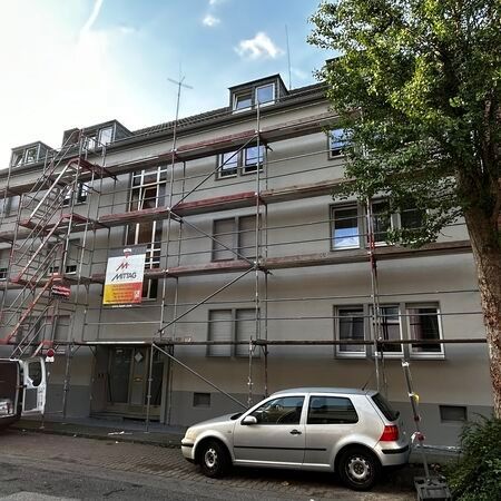 Gebäudefassade mit Gerüst, davor geparktes Auto; im Bau.