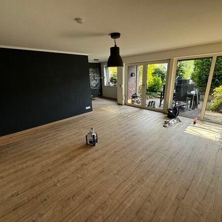 Leerer Raum mit Holzboden, schwarzer Akzentwand und Glastüren, die sich zu einem Garten öffnen.