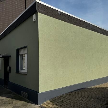 Grünes Gebäude mit dunkelgrauen Zierelementen, Fenster und Eingang.