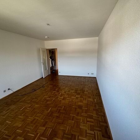 Leeres Zimmer mit Parkettboden, weißen Wänden und offener Tür.