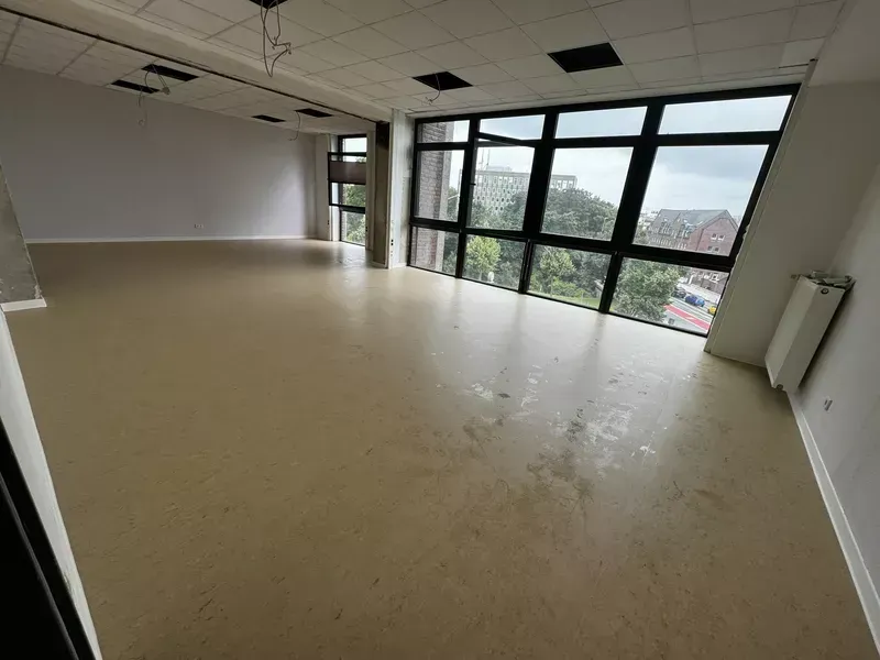 Leere Büroräume mit großen Fenstern und beigefarbenem Fußboden.