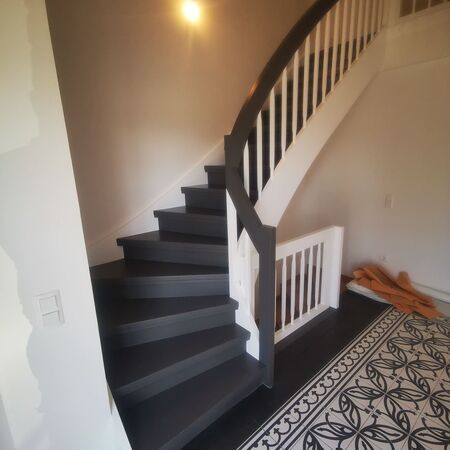 Dunkelgrau gestrichene Treppe mit weißem Geländer und gemustertem Boden.