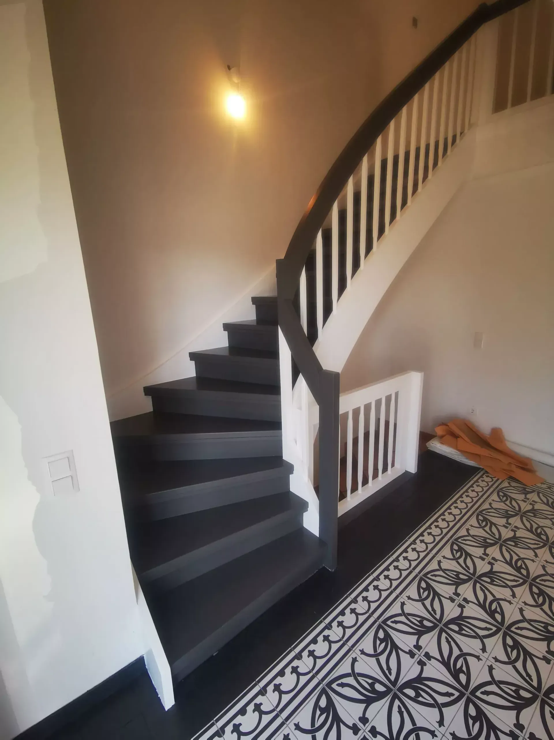 Treppe mit dunkelgrauen Stufen und weißem Geländer, die nach oben führt. Dekorativer Fliesenboden.