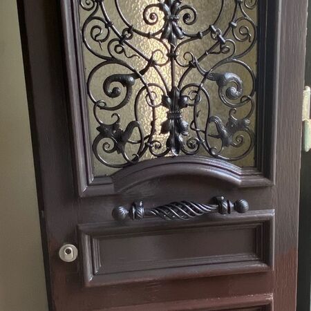 Braune Holztür mit dekorativem schmiedeeisernen Fenster und Griff.