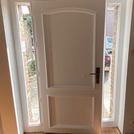 Weiße Tür mit gewölbtem Oberteil und Seitenfenstern, eingefasst in eine Ziegelumrandung.