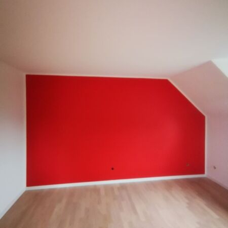 Zimmer mit roter Akzentwand, weißer Decke und Wänden sowie hellem Holzboden.