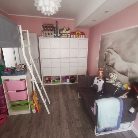 Kinderzimmer mit rosa Wänden, Etagenbett, weißen Aufbewahrungswürfeln und einem grauen Sofa mit Stofftieren.